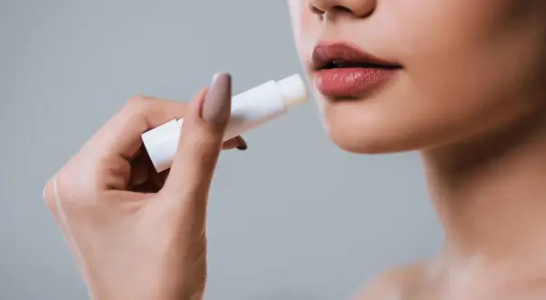 Mano applica balsamo labbra per levigare le rughe, come un codice a barre che scompare.