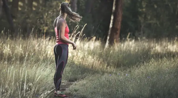 Frau im Laufoutfit im Wald. Sie genießt die Natur und die Ruhe, die das Joggen mit sich bringt.
