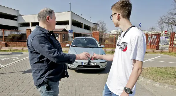 Mężczyźni przekazują sobie kluczyki do samochodu, co symbolizuje umowę użyczenia.