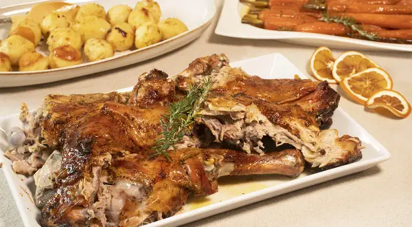 Pierna de cordero lechal al horno jugosa, dorada y tierna, acompañada de patatas asadas y zanahorias glaseadas.