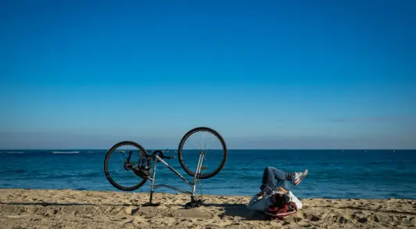 Odpoczynek po przejażdżce Velo Baltica. Rower na plaży, człowiek leży na piasku, patrząc na morze.
