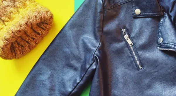 Veste en simili cuir noire et bonnet jaune sur fond coloré. Apprenez comment nettoyer une veste en simili cuir pour qu'elle reste comme neuve.