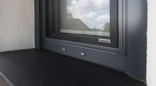 Szczelne uszczelnienie parapetu zewnętrznego okna DAKO. Ciemny parapet i szara rama okna zapewniają estetykę i ochronę.