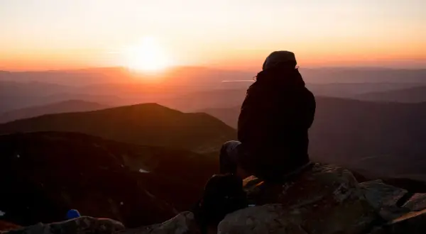 Sonnenuntergang in den Hohen Tatra. Eine Person sitzt auf einem Felsen und blickt auf die Berge.