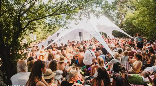 Tłum ludzi siedzi pod białym namiotem na festiwalu Wibracje, słuchając wystąpienia.