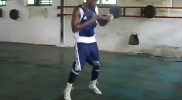 A boxer trains in a sparse gym, practicing his moves with a determined look. The scene evokes a sense of dedication, reminiscent of soviet style boxing.
