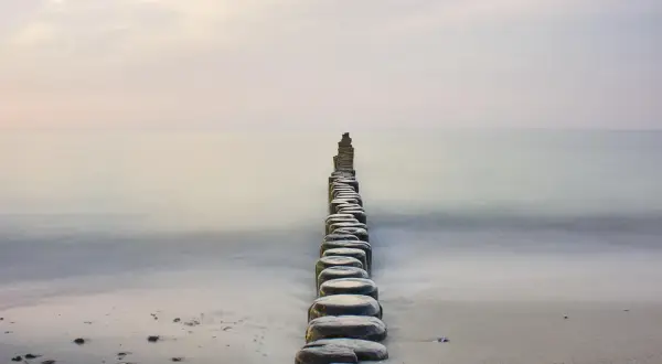 Linia drewnianych pali na plaży, prowadząca w spokojne morze, tworzy stan zen.