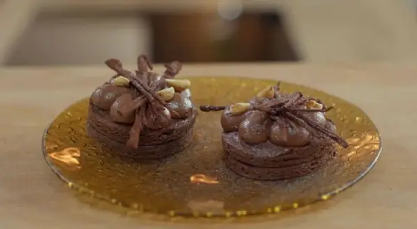 Dos bizcochos sin harina de chocolate, decorados con crema y avellanas, sobre un plato dorado.