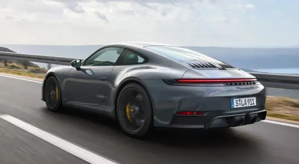 Szary Porsche 911 GTS pędzi po krętej drodze z widokiem na morze.