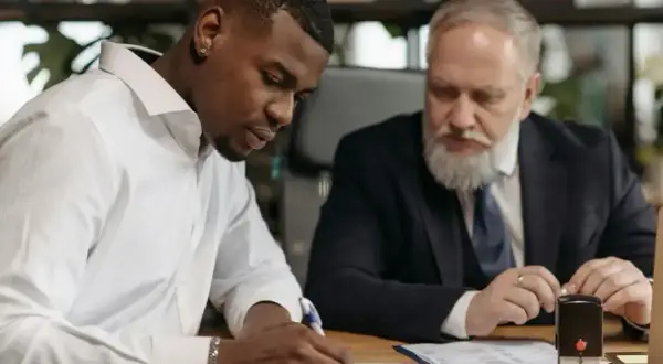Młody mężczyzna podpisuje dokumenty, podczas gdy starszy kolega przygląda się. Czy można złożyć wypowiedzenie w środku miesiąca?
