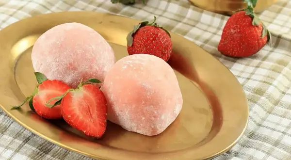 Różowe mochi z truskawkami na złotym talerzu.