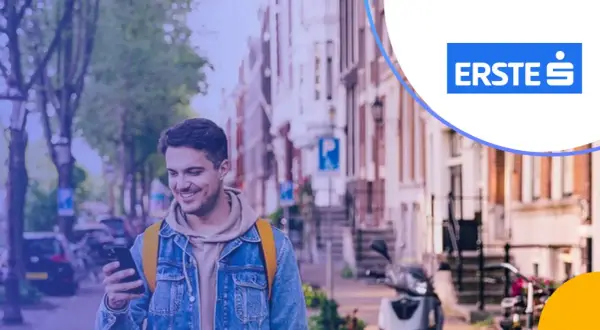 Uśmiechnięty mężczyzna z telefonem w ręku, w tle ulica z budynkami i skuterem. Promocja Santander lokata 3-miesięczna.