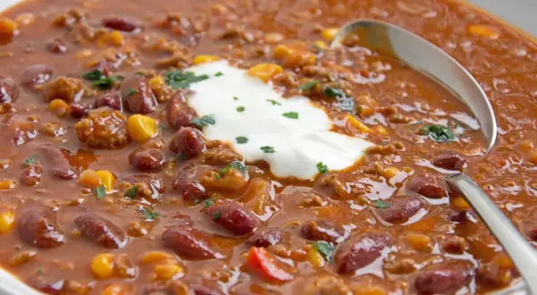 Herzhaftes Chili con Carne original mit Kidneybohnen, Mais und Hackfleisch, garniert mit einem Klecks saurer Sahne und Petersilie.
