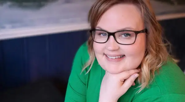 Kvinna med glasögon och grön tröja ler, trots morgonens ångest och depression.