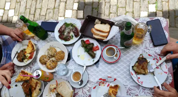 Pyszne albania jedzenie: mięso, gołąbki, placki i pieczywo na stole, obok piwo i kawa.