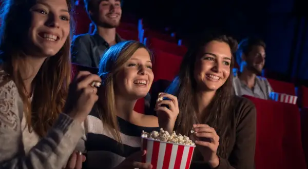 Uśmiechnięci ludzie w kinie, jedzący popcorn. Czy to Cinema City bilet rodzinny co to?
