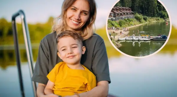 Uśmiechnięta mama z synkiem na pomoście. W tle jezioro z łódkami i domkami, idealne miejsce na wykorzystanie bonu turystycznego.