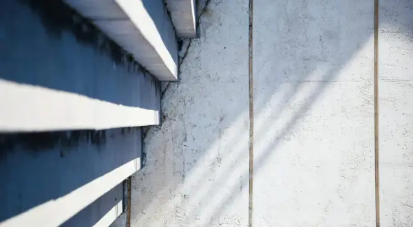 Ombre et lumière sur un mur en béton cellulaire, révélant des traces d'humidité et de légères fissures.