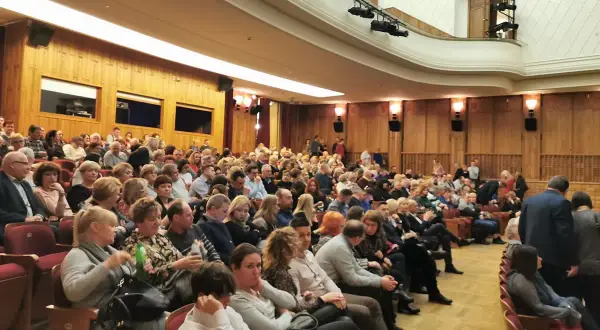 Widownia w teatrze, ludzie siedzą w rzędach, ubrani elegancko.