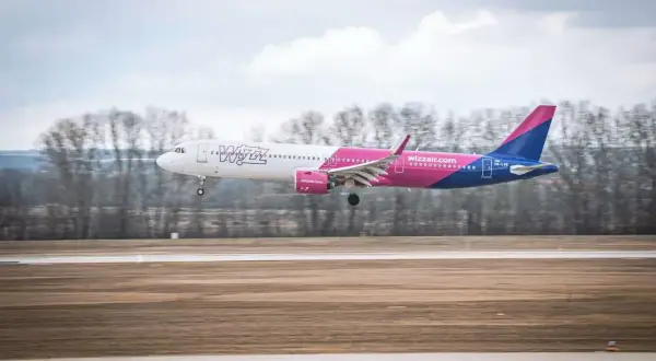 Samolot Wizz Air z różowym ogonem ląduje na pasie startowym. Wizz rozkład miejsc w samolocie Wizzair jest dobrze widoczny.
