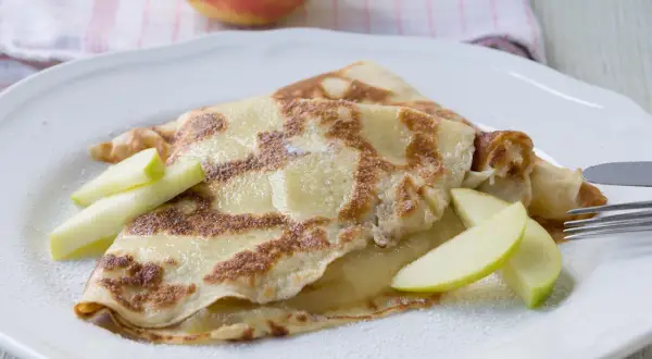 Zwei goldbraune Pfannkuchen mit Apfelmus gefüllt, garniert mit Apfelspalten und Puderzucker.