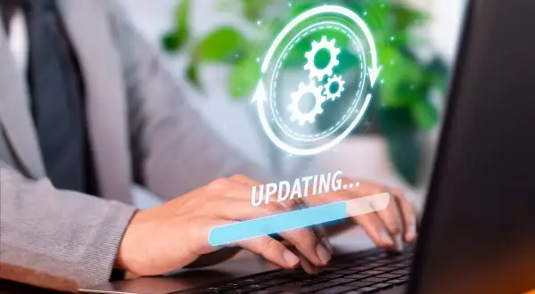 Osoba w garniturze pracuje na laptopie, na ekranie widoczny pasek postępu "UPDATING..." i ikona aktualizacji. Dowiedz się, jak zaktualizować Windows 10.