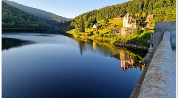 Spokojna tafla jeziora odbija zamek i zalesione wzgórza czeskich Karkonoszy.