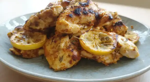 En tallrik med saftig, grillad marinera kyckling med citronskivor. Perfekt för en lätt och smakrik måltid.