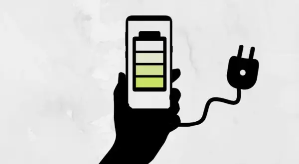 Mano sosteniendo un teléfono con batería a 3/4, conectado a un enchufe. ¡Un truco para el ahorro de batería!