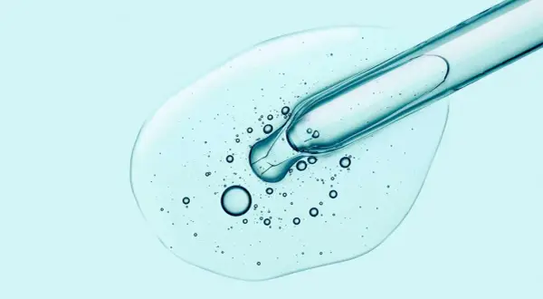 Tropfen Hyaluron-Serum aus Pipette auf hellblauem Hintergrund. Hilft gegen Pickel und spendet Feuchtigkeit.