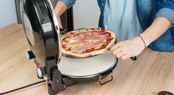 Osoba wkłada pizzę z szynką do pieca. Szybko i łatwo przygotujesz idealne danie.