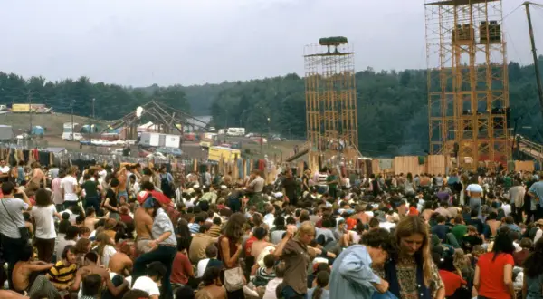 Tłum ludzi na festiwalu, gdzie jest Woodstock? Widać scenę, wieże głośnikowe i namioty.