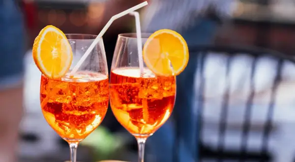 Dos Aperol Spritz refrescantes, con rodajas de naranja y pajitas, evocan el aperitivo italiano y su aperol spritz origen.