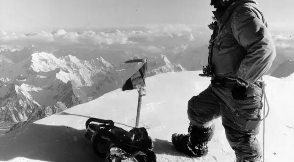 Bergsteiger auf dem Gipfel des K2, der die Erstbesteigung feiert. Ausrüstung und Fahne im Schnee.