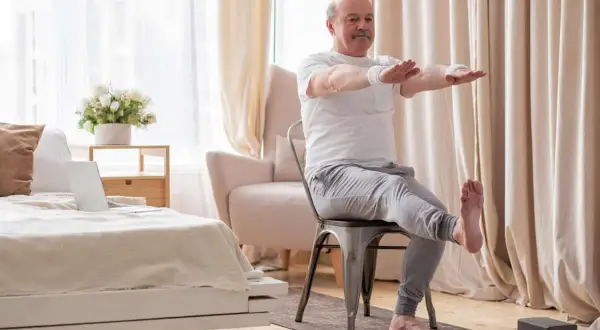 Starszy mężczyzna ćwiczy odwodziciele uda, siedząc na krześle w salonie.