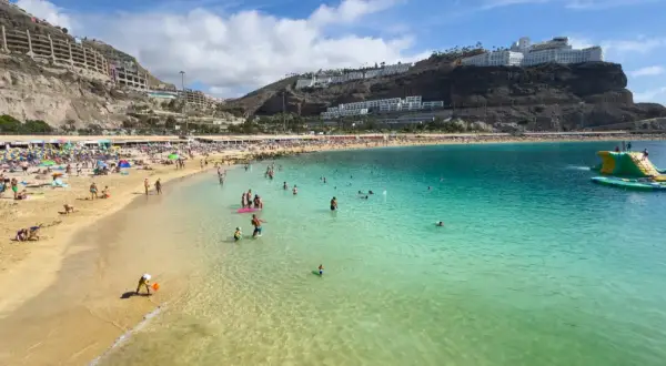 En livlig strand på Gran Canaria med solbadare, badande och en uppblåsbar vattenpark. En perfekt dag för att njuta av solen och havet.