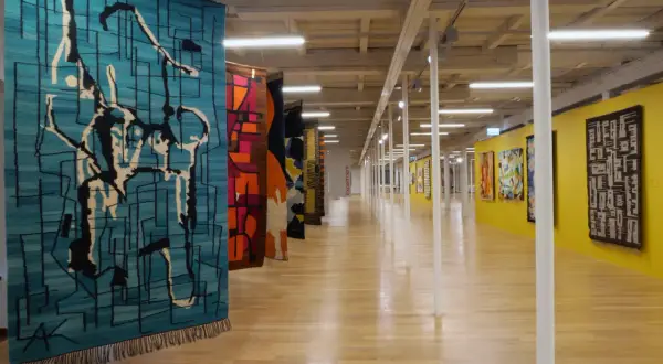 Wystawa prezentuje, kto wytwarza dekoracyjne tkaniny ścienne. Kolorowe, abstrakcyjne wzory zdobią galerię.