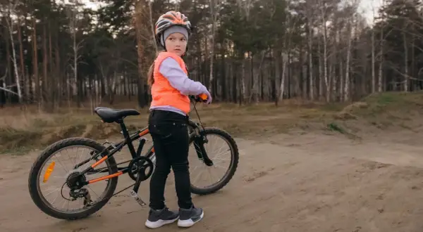 Dziewczynka w kasku i kamizelce pomarańczowej stoi obok roweru, gotowa na egzamin na kartę rowerową.