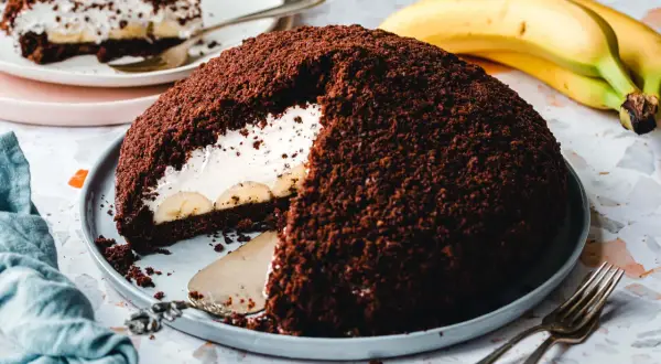 Ein saftiger veganer Maulwurfkuchen mit Bananen und Sahne, bedeckt mit Schokoladenkrümeln.
