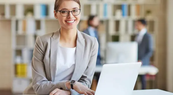 Lächelnde Frau mit Brille am Laptop, bereit für ihre medizinische Schreibkraft Ausbildung.