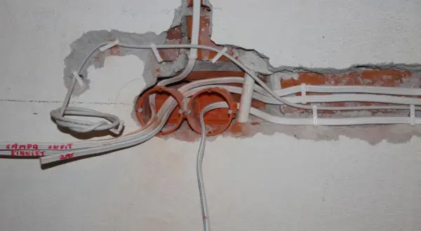 Rozpoczęta wymiana instalacji elektrycznej: widoczne puszki, przewody i fragmenty ceglanej ściany.