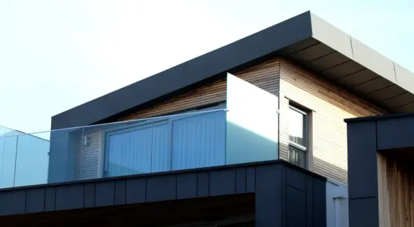 Nowoczesny budynek z drewnianą elewacją i szklanymi balustradami. Widać fragment dachu, który sugeruje, jak zrobić spadek na dachu płaskim.