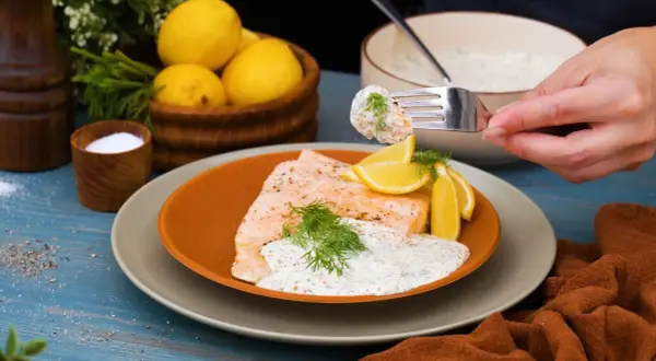 En bit lax med romsås, citronklyftor och dill. En gaffel med lax och sås lyfts från tallriken.
