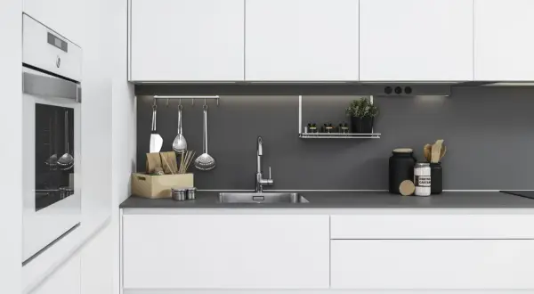 Moderna cocina blanca y gris con electrodomésticos integrados, fregadero de acero inoxidable y utensilios de cocina colgados.