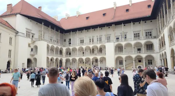 Tłum turystów zwiedza dziedziniec Wawelu, podziwiając renesansową architekturę. Warto zobaczyć na Wawelu to miejsce pełne historii.