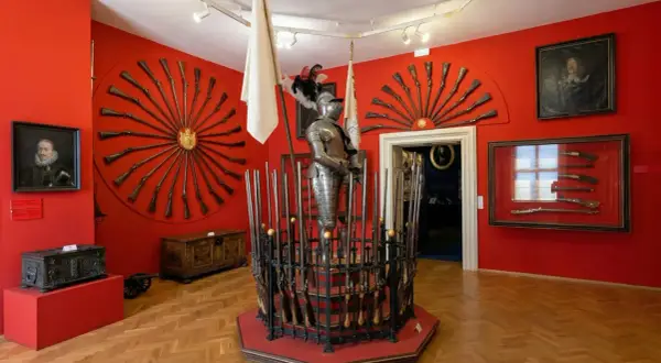 Armure de chevalier et fusils anciens exposés dans une salle rouge vif, un aperçu de l'interieur chateau de Prague.