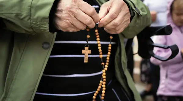 Dłoń starszej osoby trzyma paciorki różańca, odmawiając modlitwę do anioła stróża za dorosłe dzieci.