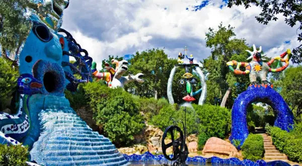 Sculture colorate e fantastiche popolano il **giardino dei tarocchi**, tra alberi verdi e cielo nuvoloso.