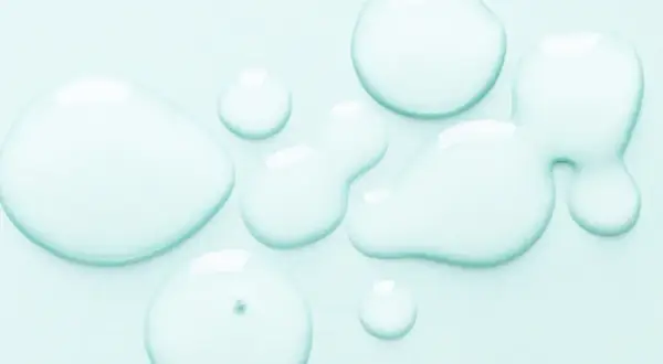 Gocce trasparenti su sfondo azzurro. Alcuni si chiedono se il cocamidopropyl betaine fa male, ma questa immagine mostra solo liquidi puri.