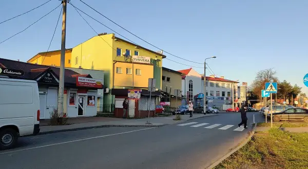 Ulica w Kleosinie z kolorowymi budynkami, sklepami i przejściem dla pieszych.
